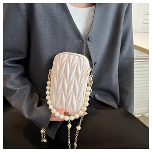 Detail of cream quilted phone bag with pearl handle and metal chain on a grey blazer
