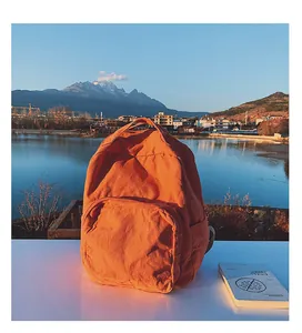 Dettaglio di uno zaino in tela arancione brillante con ampia tasca frontale e porta borraccia