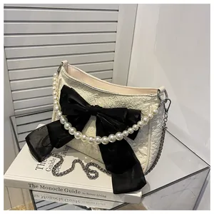 Dettaglio borsa in tessuto crema con fiocco nero, manico di perle e catena