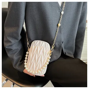 Detail of a quilted crossbody phone bag with pearl handle and gold chain strap