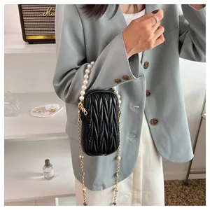Quilted black mini crossbody bag with pearl handle and gold chain strap on female model