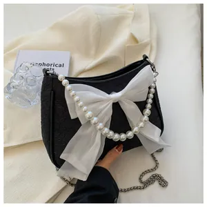 Dettaglio borsa a tracolla in tessuto nero con fiocco in organza e catena di perle