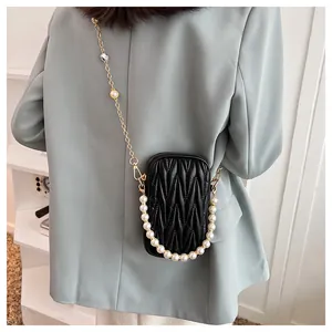 Detail view of black quilted mini bag with gold chain and decorative pearl strap