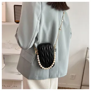 Detail of black matelassé crossbody bag with gold chain and pearl strap on model