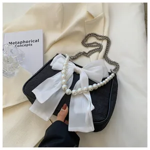 Dettaglio borsa a tracolla nera con fiocco in chiffon e manico di perle eleganti