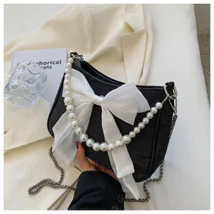Dettaglio della borsa nera in tessuto con grande fiocco di seta bianco e catena di perle