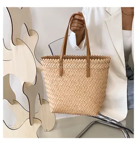 Detail of woven straw tote bag with brown leather handles and metallic rivet reinforcement
