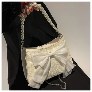 Dettaglio borsa a tracolla crema con fiocco grande e manico in perle eleganti