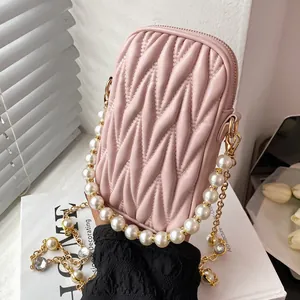 Pink quilted crossbody phone bag with pearl chain strap and gold hardware shown in hand