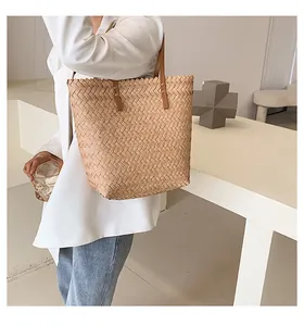 Close-up of woven straw tote bag with brown leather handles and metal rivets