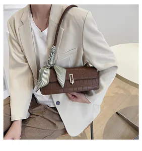 Dettaglio borsa marrone effetto coccodrillo con foulard di seta a righe verdi e fibbia d'oro