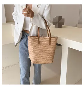 Close-up of woven straw tote bag with scalloped edge and leather shoulder strap handles