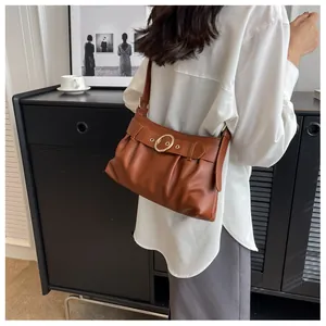 Borsa a spalla arricciata marrone con fibbia dorata su modella con camicia bianca