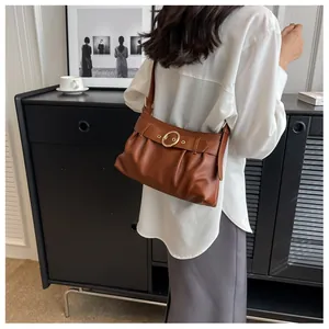 Dettaglio di una borsa a spalla marrone increspata con fibbia dorata e camicia bianca