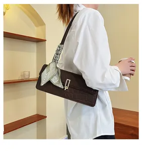 Dettaglio di una borsa a tracolla marrone coccodrillo con fibbia d'oro e foulard in seta