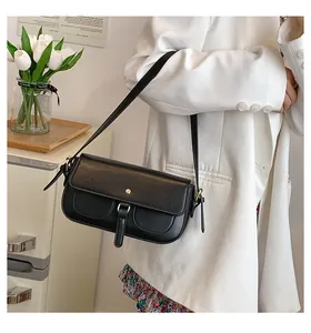 Dettaglio di una borsa a tracolla in pelle nera opaca con hardware dorato indossata da una modella