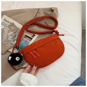 Dettaglio di una borsa a tracolla in tela arancione con spalline intrecciate e ciondolo