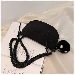 Dettaglio di una borsa a mezzaluna nera in tela con tracolla intrecciata e ciondolo