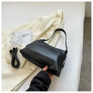 Dettaglio borsa hobo nera a pieghe con tracolla regolabile su sfondo di abito beige