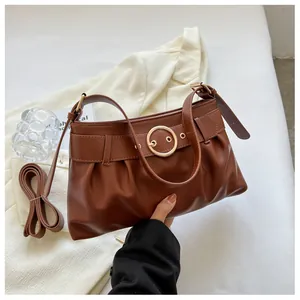 Dettaglio borsa in pelle marrone con fibbia dorata, pieghe e tracolla regolabile