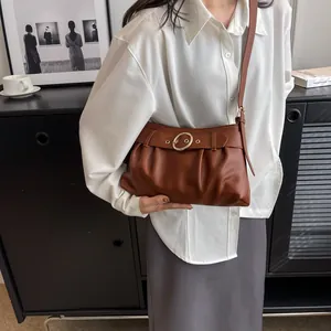 Borsa sottobraccio arricciata marrone con fibbia dorata su modella in un set minimalista