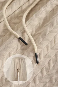 Detail of beige men's jacquard shorts with drawstring and textured fabric pattern