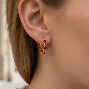 Macro shot of gold floral earrings with three vertical red zircons on model ear