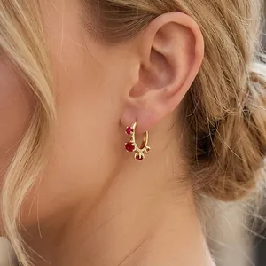 Detail of 18K gold hoop earring with three red zircons worn by a model in soft light
