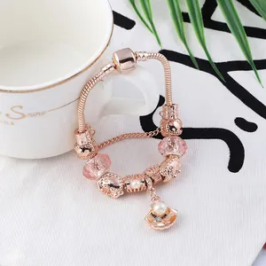 Rose gold snake chain bracelet with pearl shell charms and hollow beads on a white fabric