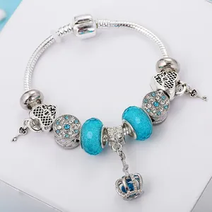 Silbernes Schlangenarmband mit blauen Perlen und funkelndem Kronenanhänger auf weißem Grund