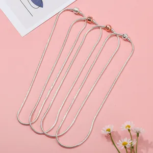 Vue détaillée de quatre chaînes serpent en argent et or rose sur un fond rose pastel