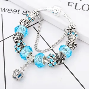 Macro detail of blue faceted glass beads and silver crown pendant on snake chain bracelet