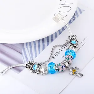 Detail van een slangenarmband met blauwe kristallen en vlinder en bloem hangers