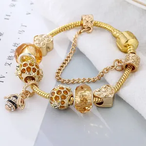 Détail du bracelet doré avec breloques d'abeilles, perles ambrées et pendentif cœur