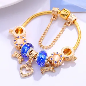 Goldenes Charm-Armband mit blauen Glasperlen und Schleifenanhängern auf weißem Grund