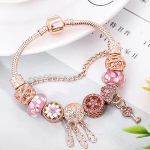 Roségoldenes Schlangenarmband mit Herz-, Schlüssel- und Traumfänger-Anhängern auf Tablett