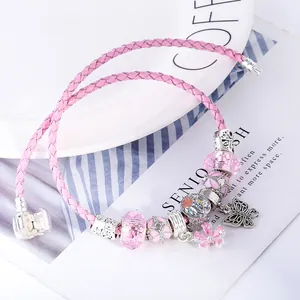 Pink double-layer leather charm bracelet with floral and butterfly pendants on white plate