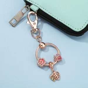 Macro detail of rose gold keychain with rhinestone flower and leaf charms on blue surface