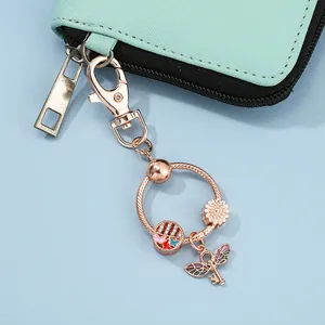 Close-up of rose gold keychain with sunflower and wing key charms on mint green wallet