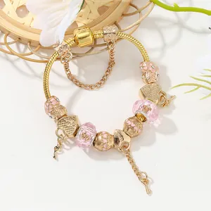 Goldenes Schlangenarmband mit rosa Herzanhängern und Schlüssel in einer floralen Schale