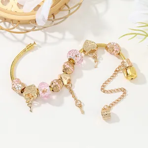 Goldenes Charm-Armband mit rosa Glasperlen, Herzanhängern und Schlüssel auf Naturhintergrund