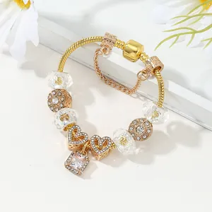 Bracciale a catena serpente dorata con ciondoli a cuore e perle di cristallo su sfondo bianco