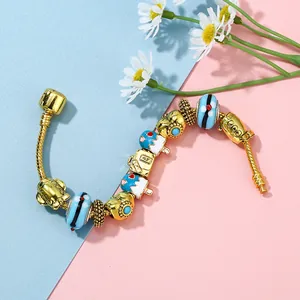 Gouden slangarmband met blauwe glazen kralen en uilenbedeltjes op een pastelkleurige achtergrond