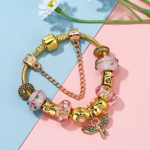 Bracciale dorato con charm, perle di vetro rosa e un ciondolo a forma di chiave alata