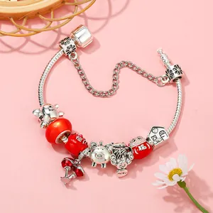 Silver snake chain bracelet with red fortune bag and lucky cat charms on pink background