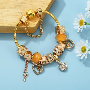 Golden snake chain bracelet with orange beads and hollow heart charms on blue backdrop