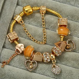 Macro shot of gold snake chain bracelet with heart rhinestone charms and orange glass beads