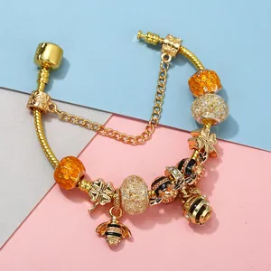 Gold bee and clover charm snake chain bracelet with amber glass beads on color background