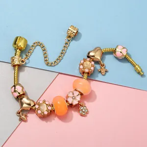 Detail of golden snake chain bracelet with pink flower and cute bee charms