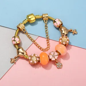 Golden charm bracelet with pink flowers, bees, and heart pendants on a tricolor background